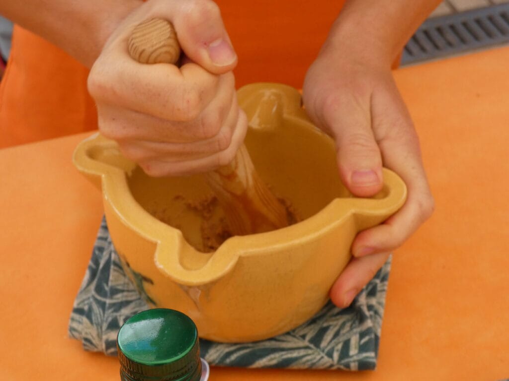 Persona triturando ingredientes en un mortero para preparar salsa de Xató.