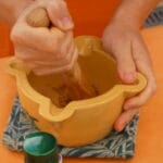 Persona triturando ingredientes en un mortero para preparar salsa de Xató.