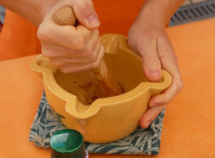 Persona triturando ingredientes en un mortero para preparar salsa de Xató.